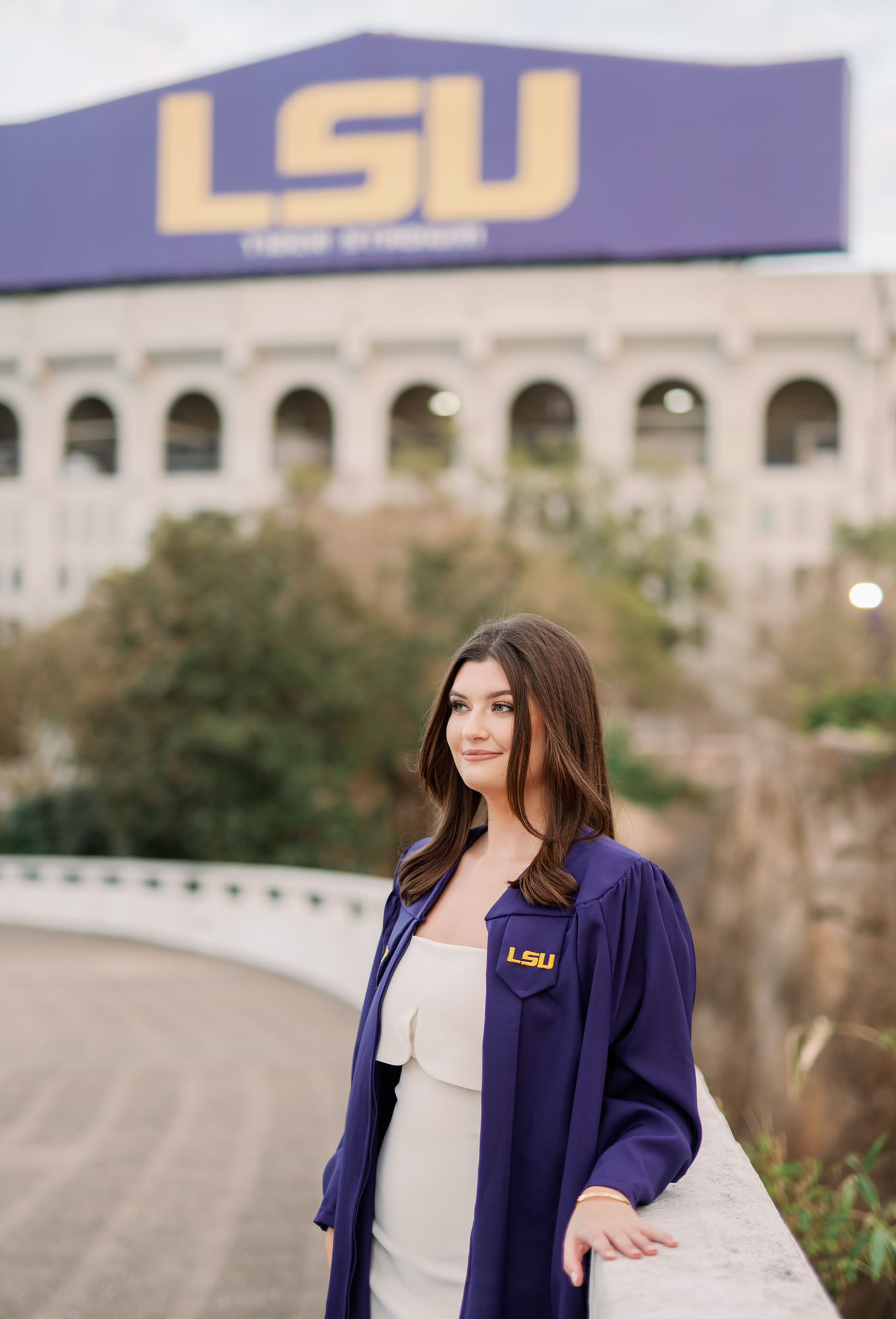 Madison Menou in graduation gown on LSU campus with Tiger Stadium in the background.